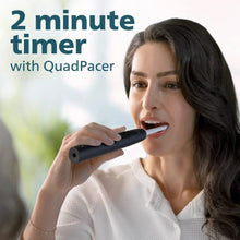 Black rechargeable toothbrush held near mouth with white bristle head