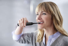 Person using Philips Sonicare electric toothbrush, black handle with bristles