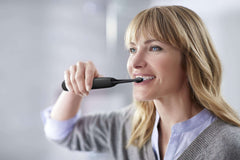 Woman brushing teeth with Philips Sonicare 4300 electric toothbrush UAE in bathroom mirror