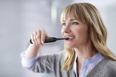 Woman brushing teeth with Philips Sonicare 4300 electric toothbrush UAE in bathroom mirror