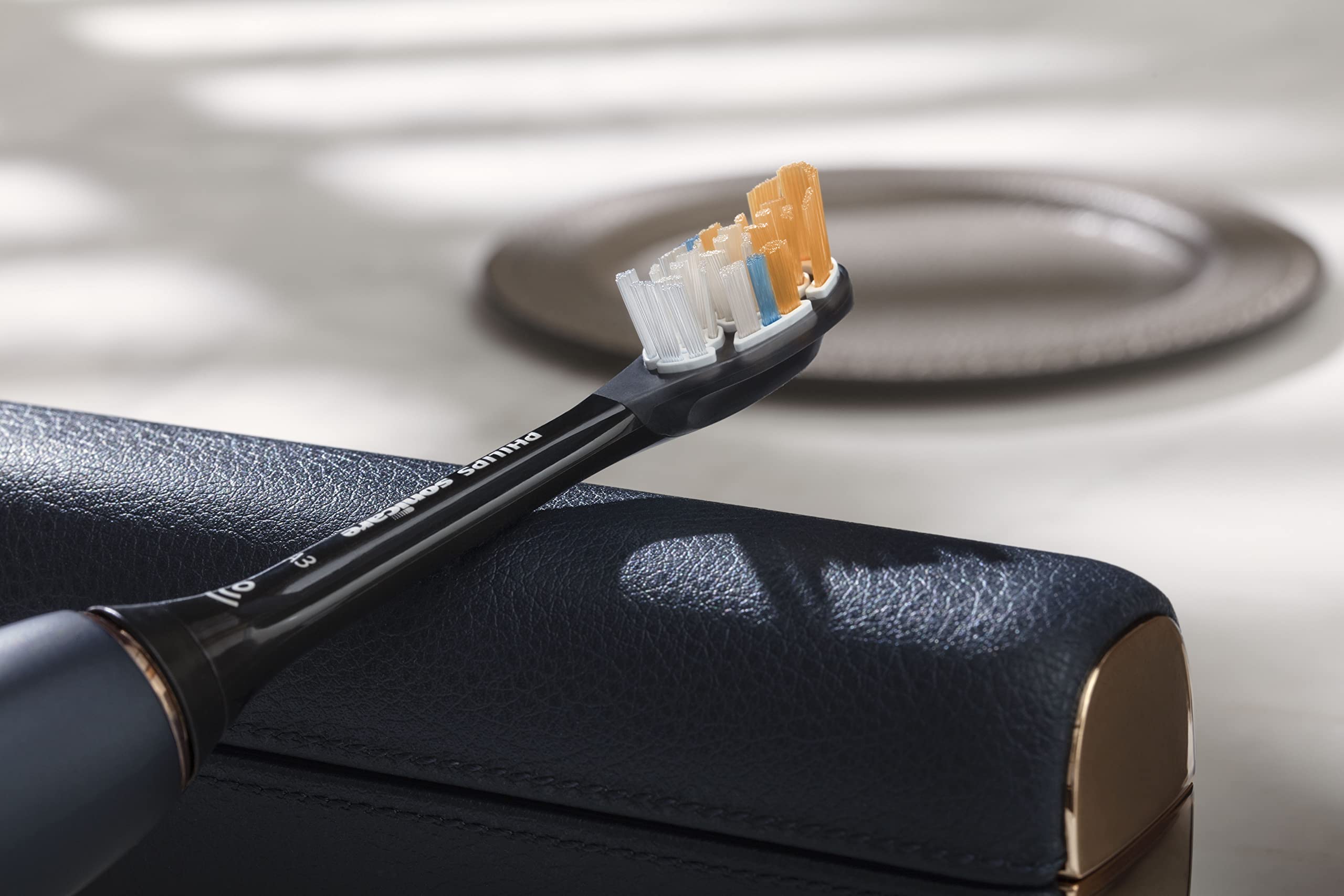 Philips Sonicare 9900 Prestige toothbrush with charcoal handle and replacement brush head resting on leather travel case
