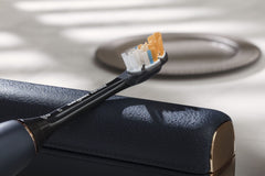 Philips Sonicare 9900 Prestige toothbrush with charcoal handle and replacement brush head resting on leather travel case