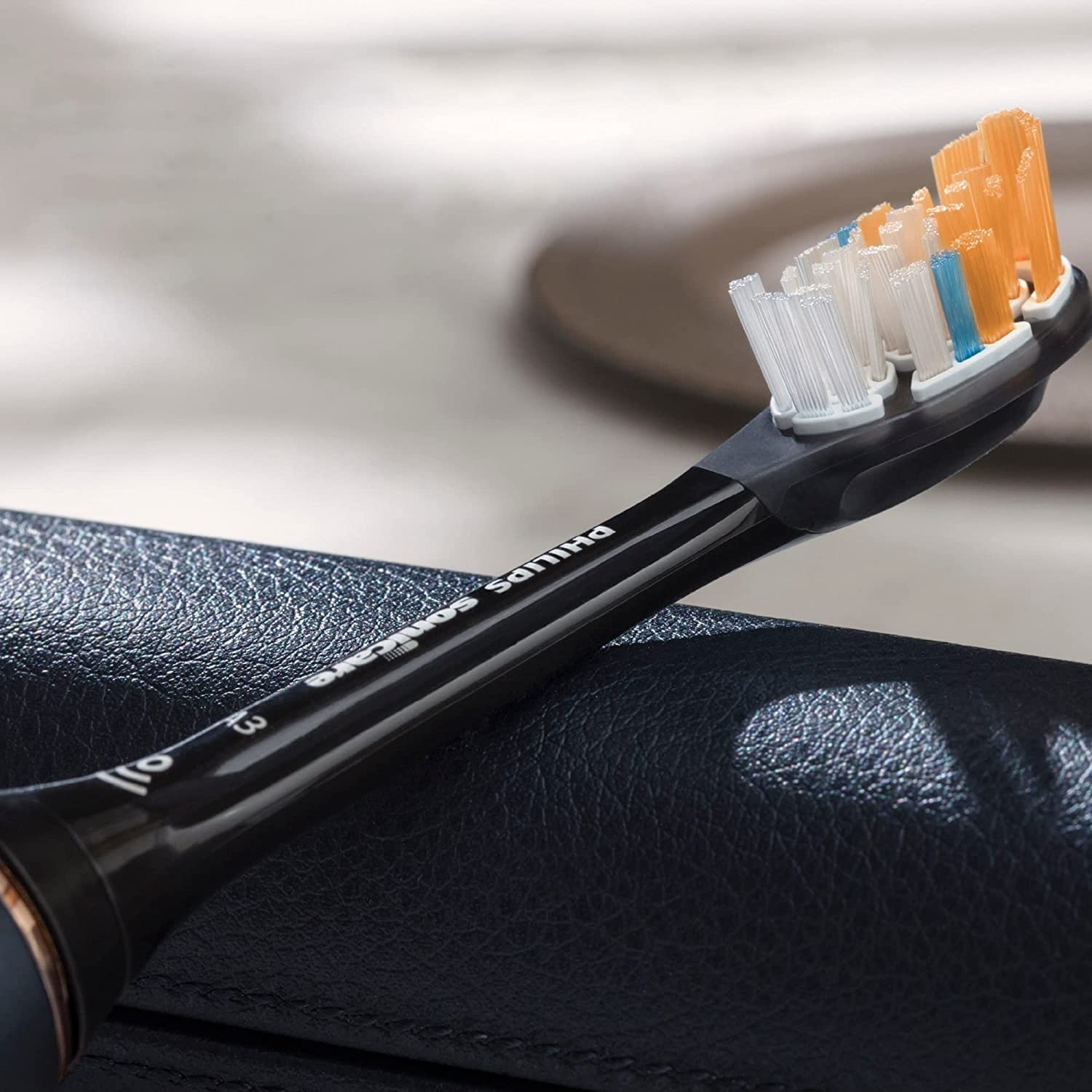 Black electric replacement head with white blue and orange bristles on textured surface Philips Sonicare Premium brush heads