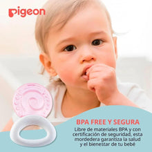 Pink circular cooling teether with white ring handle near a baby’s hand