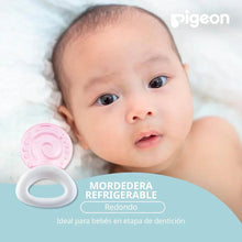 Pink circular cooling teether with white ring handle beside a baby on a mat