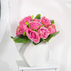 Pink artificial rose bouquet arranged in a white geometric vase with green leaves