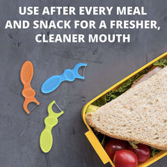 Three colorful Plackers dual grip dental flossers next to a lunchbox with sandwich and tomatoes for after meal flossing