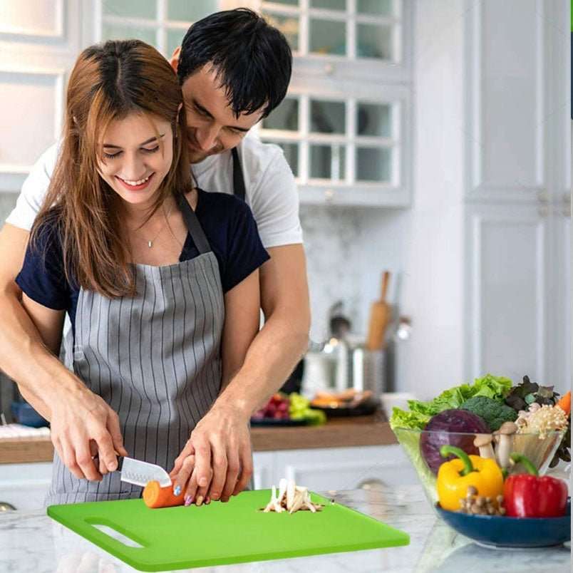 Couple using a green plastic chopping board with handle to cut vegetables in a modern kitchen