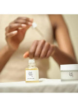 Facial serum bottle and cream jar on table with person applying drops from dropper