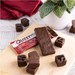 Quest chocolate brownie protein bars unwrapped on wooden board with brownie pieces and plant backdrop