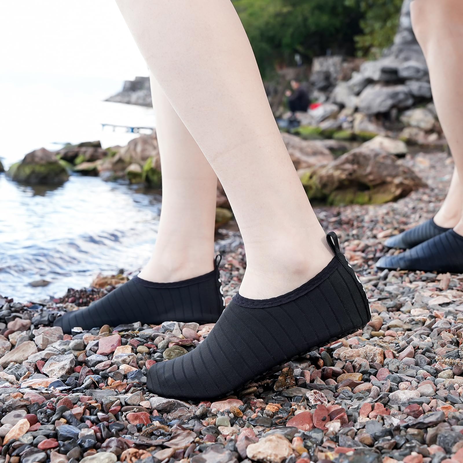 Black quick dry water shoes for adults worn on rocky beach with water in background