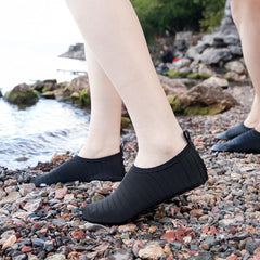 Black quick dry water shoes for adults worn on rocky beach with water in background