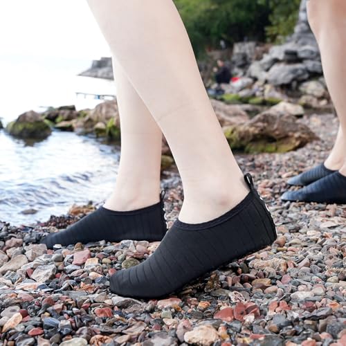 Black quick dry water shoes for adults worn on rocky shore near water
