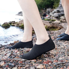 Black quick dry water shoes for adults worn on rocky shore near water