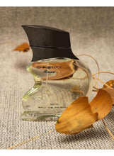 Eau de Parfum bottle with dark cap and gold-toned label, 100 ml, clear glass.