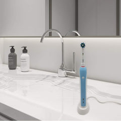 Blue electric toothbrush on white Oral b electric toothbrush charger UK on bathroom countertop by faucet and soap bottles