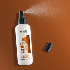 Revlon Uniq One Coconut Hair Treatment spray bottle with nozzle spraying mist on brown background