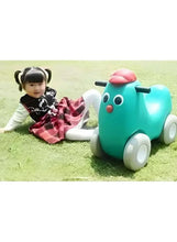 Teal kid ride-on car toy with pink dome, used outdoors on grass with child
