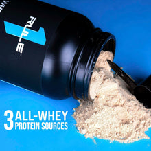 Black whey protein tub pouring light-colored protein powder from the open scoop.