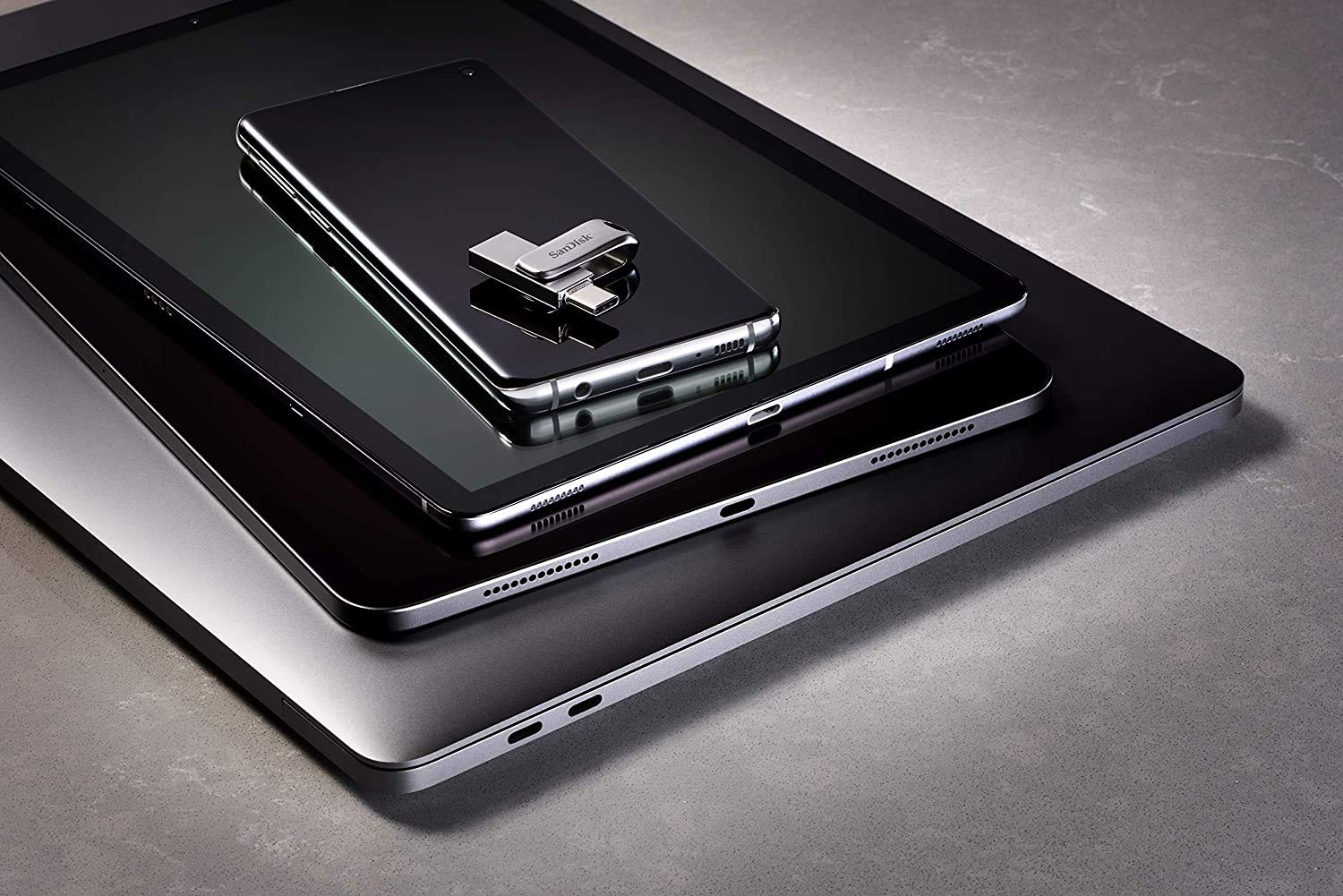 SanDisk 512GB USB Type-C drive placed on top of a smartphone, tablet, and laptop showing portable storage