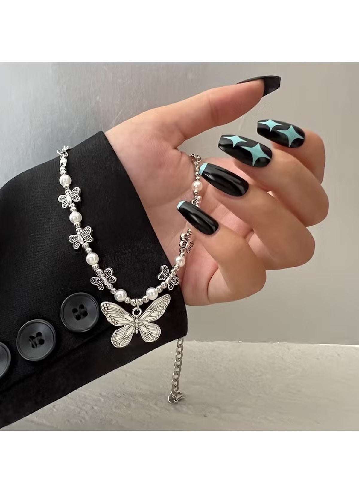 Huitich silver butterfly pendant necklace with floral and pearl accents worn on hand with black star nail art