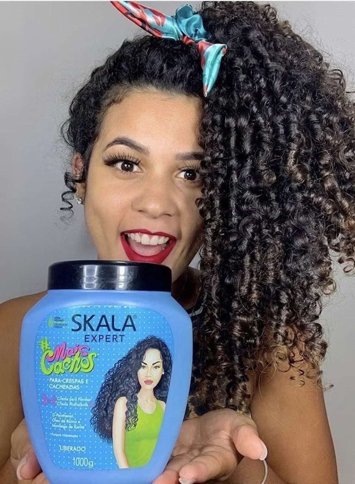 SKALA curl defining hair cream in a blue jar held by a woman with curly hair