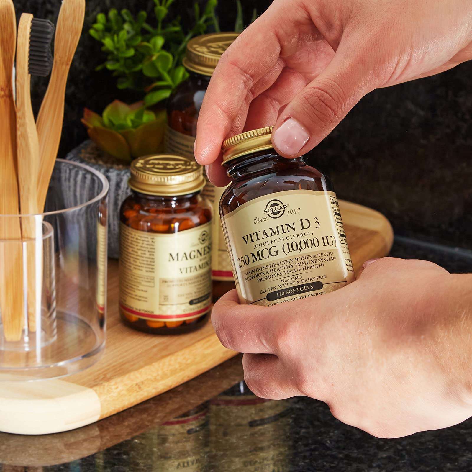 Hands opening amber bottle of Solgar Vitamin D3 softgels on kitchen counter with other supplement jars