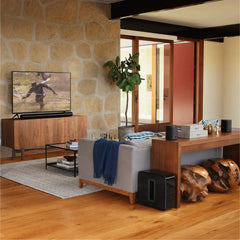 Premium smart soundbar for TV placed below a flat screen in a modern living room with wooden furniture