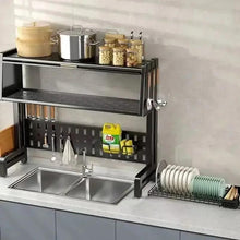 Black two-basin sink rack with open drying shelf, utensil pegs, and stacked dishware
