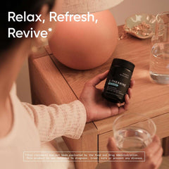 Hand holding Sports Research L-theanine softgels bottle by bedside table with glass of water and lamp