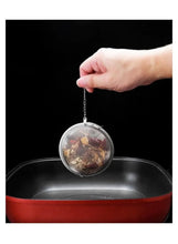 Stainless steel mesh tea infuser ball hanging from a chain over a pot