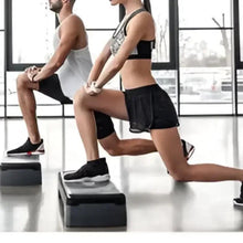 Black fitness step platform used by two people for step-ups in a gym