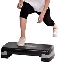 Black fitness step platform with textured top, used for home workout exercises