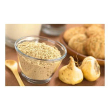 Glass bowl of beige maca powder with maca root pieces on wooden spoon