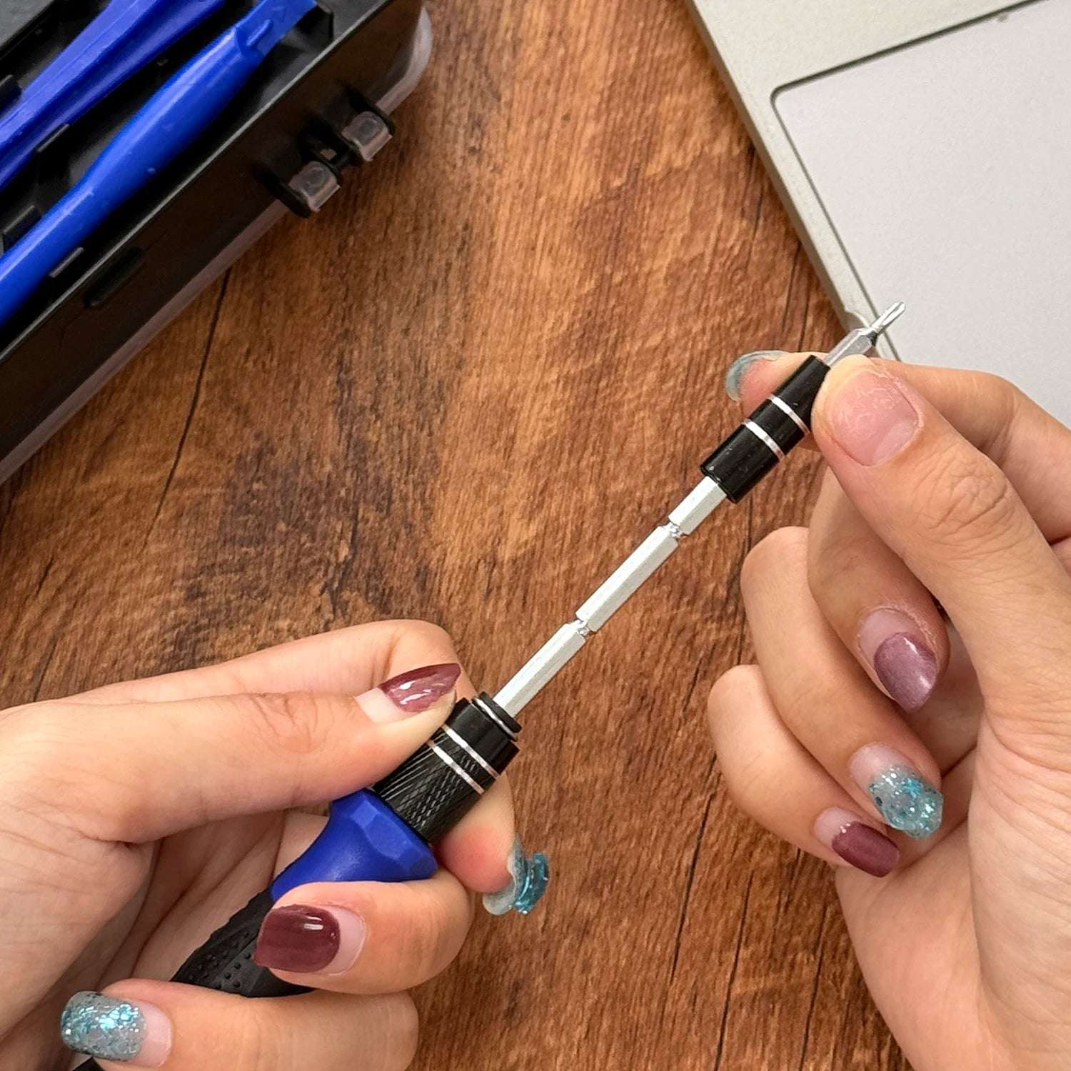 Mumzar precision screwdriver set for electronics shown with hands swapping bits near laptop on wood surface