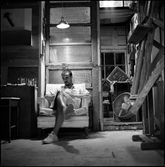 Black and white photo of a man reading The Day The Crayons Came Home book while sitting on a chair in a rustic room