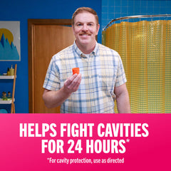 Man in bathroom holding orange rinse cup and smiling with TheraBreath oral rinse for bad breath label and cavity protection text