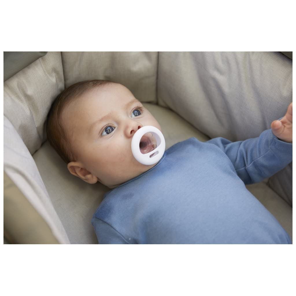 Newborn in blue onesie lying in bassinet using Tommee Tippee breast-like pacifier white shield nipple closeup