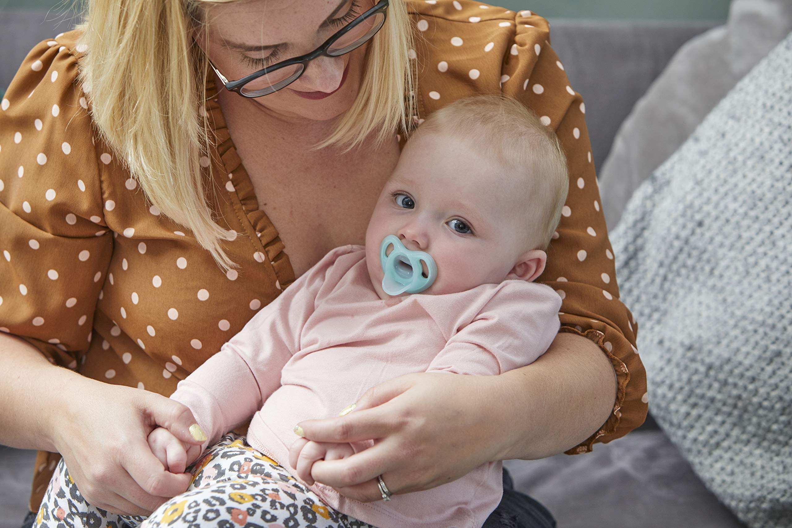 Mother cradling baby on couch with Tommee Tippee ultra light soother in baby mouth for comfort