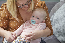 Infant with light blue silicone soother held by adult on sofa