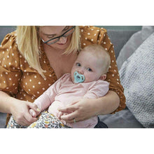 Baby with light blue silicone soother in caregiver’s arms