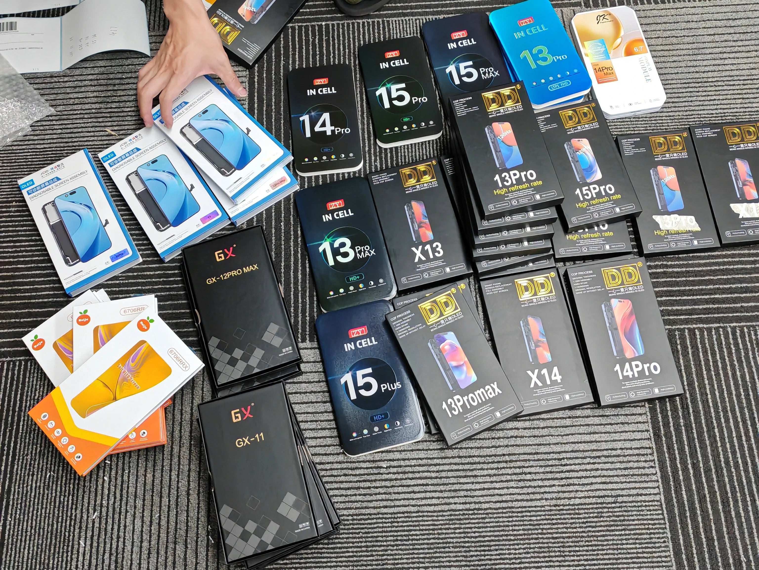 Mumzar assortment of boxed iPhone screens and parts on carpet showing multiple models iPhone OLED display replacement stock