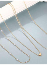 Triple-layer pearl choker necklace laid out on display with gold-tone chains and heart charm