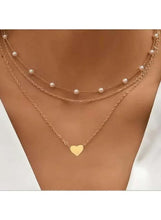 Triple-layer pearl choker necklace on neck with gold-tone chains, white pearls, and heart charm