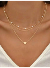 Triple-layer pearl choker necklace with gold-tone chains, white pearl beads, and heart charm