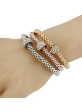 Triple tone crystal bracelets on wrist: rose, silver, and gold woven chain with charms
