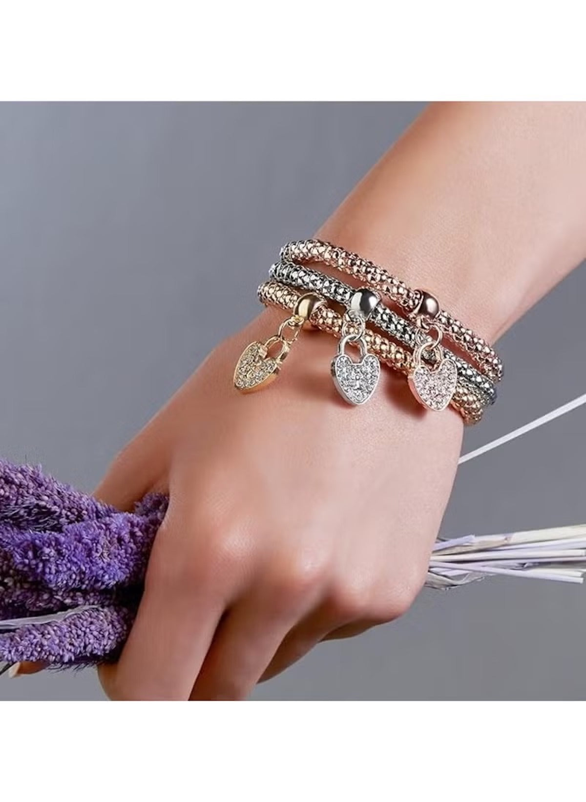 Huitich triple tone love charm bracelets with heart pendants worn on wrist holding purple flowers