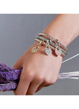 Stacked triple-tone charm bracelets on wrist with small heart charms and clasp links