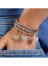 Triple-tone beaded bangles bracelet on wrist with dangling heart charms in silver, gold, rose
