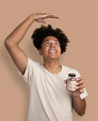 Smiling teen holding TruHeight supplement bottle while measuring his height gesture showcasing height growth gummies for kids